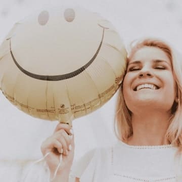 Lachende Frau mit einem Luftballon in der Hand. Auf dem Luftballon ist ein lachender Smiley zu sehen